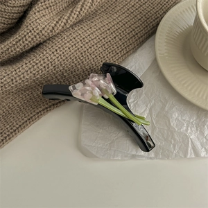 Detail of a black Calla Lily hair claw clip with pink floral decor on white paper