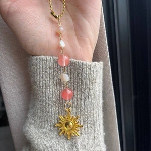 Golden sun pendant crystal ornament with pink beads and white pearl held in hand