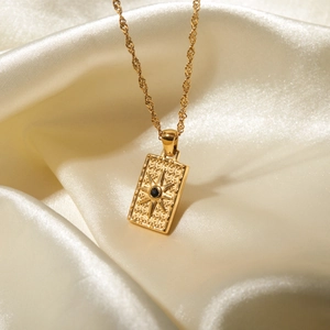 Detailed macro of golden twist chain with square star pendant and black zircon on silk