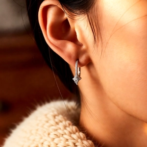 Silver star drop earrings with sparkling zircons shown on ear with a cozy beige sweater