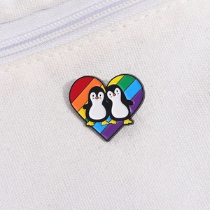 Detail of heart enamel pin with penguins and rainbow flag on white canvas background