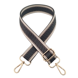 Macro view of dark grey and beige herringbone strap with gold metal hooks and buckle