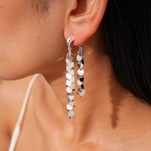 Détail de longues boucles d'oreilles à pompons argentés avec disques métalliques