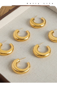 Detailed top view of gold-plated C-shaped chunky hoop earrings on a light fabric wooden tray