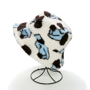 Detail view of plush cow print bucket hat in light blue and brown on a black metal stand