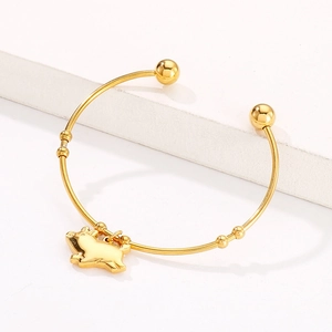 Détail d'un bracelet doré ouvert avec un pendentif cochon poli sur un support minimaliste