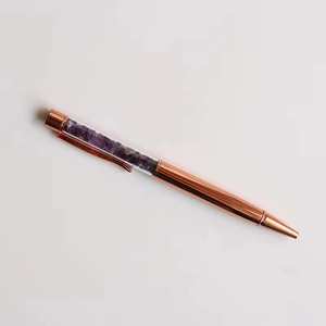 Detail of rose gold metal ballpoint pen filled with purple crystal stones in clear barrel