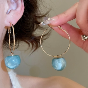Detailed close-up of golden hoop earrings with pearlescent light blue resin sphere charms