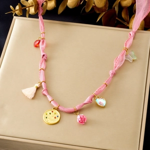 Detailed shot of a pink ribbon necklace with diverse charms on a gold gift box