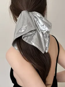 Macro detail of large metallic silver bow scrunchie showing glossy texture and finish