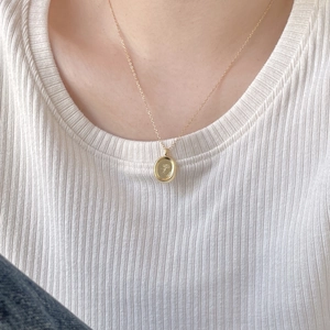 Detail of gold oval pendant necklace featuring floral relief worn over a white top