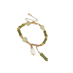 Bamboo style bracelet with green beads, golden accents and a white flower charm