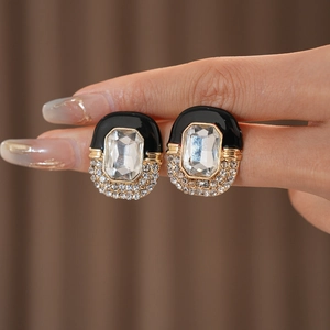 Macro shot of vintage gold earrings with crystals and black enamel details on fingers