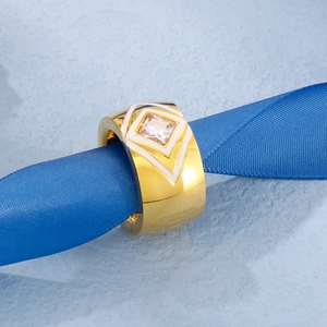 Close-up of a wide gold ring with white enamel patterns and a square cubic zirconia stone