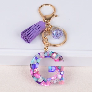 Detail of letter G resin keychain featuring purple tassel and colorful stone inlay
