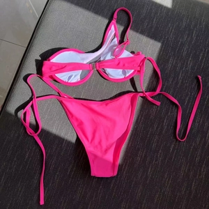Detailed flat lay of pink one-shoulder bikini with metallic buckle and tie-side bottoms