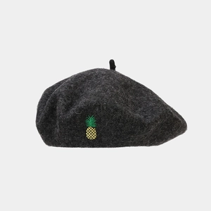 Détail d'un béret en laine gris foncé avec broderie ananas sur une surface plane