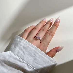 Close-up of pink heart-shaped zircon ring with diamond-encrusted silver band on a finger
