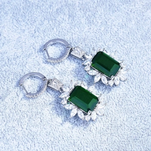 Macro shot of silver earrings with emerald cut green stones and white accent diamonds