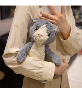 Soft plush grey and white cat doll held by a person in a cozy warm setting