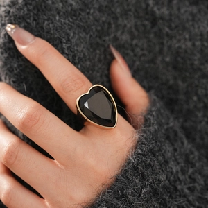 Macro shot of a large heart-shaped black faceted gemstone on a gold-plated chunky ring