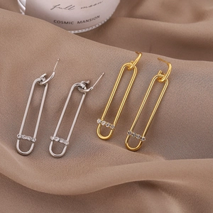Elegant safety pin earrings in gold and silver with zircon accents on brown satin