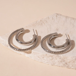 Macro detail of silver C-shape earrings with concentric circles and woven texture
