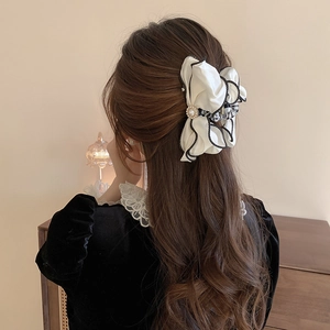 Close-up of a layered ivory satin bow hair claw clip with pearls and black pleated trim