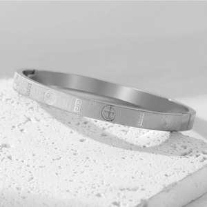Detail of silver titanium steel bangle with religious saint medals on textured stone