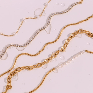 Detailansicht goldener Seilketten, Süßwasserperlen und Zirkon-Fußkettchen auf rosa Grund