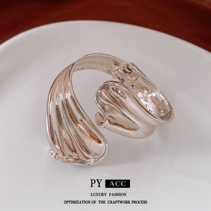 Modern twisted silver bangle with fluid design and spring clasp on a ceramic tray