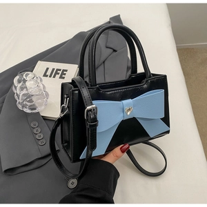 Close-up of black leather crossbody bag with a large light blue bow and heart-shaped buckle