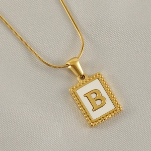 Makroaufnahme von Goldanhänger mit weißem Emaille und goldenem Buchstaben B auf Stoff