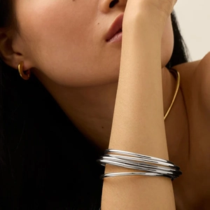 Detailed view of layered silver bangles and gold hoop earrings on a model
