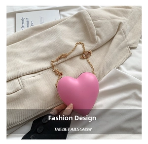 Detail shot of a pink heart-shaped crossbody bag featuring gold chain and metallic trim