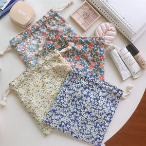 Detail of four floral cotton drawstring pouches organized on a desk with cosmetics