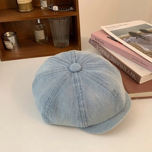 Detail shot of light blue denim newsboy cap on a desk with vintage books and accessories