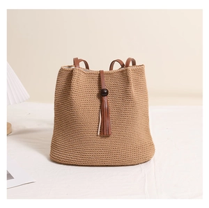 Detail of khaki woven straw bucket bag with dark brown leather strap and long tassel fringe