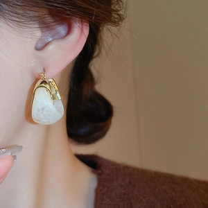 Close-up of a model wearing U-shaped gold earrings with white textured resin charms