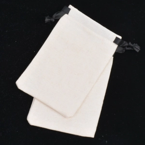 Close-up of two beige cotton linen jewelry pouches with black drawstrings on black velvet