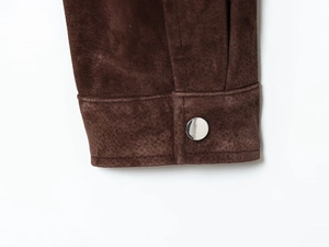 Detail of dark brown suede bomber jacket sleeve with silver metal button and stitching
