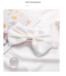 Detail of pink silk sleep mask featuring a large white bow on elegant satin background