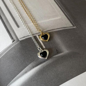Macro detail of gold and silver heart necklaces with black onyx inlay on minimal background