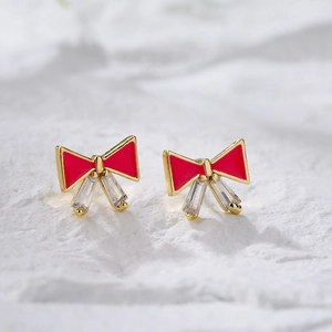 Golden bow earrings with red enamel and rectangular zircon crystals on white background