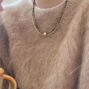 Detail of double-layer beaded necklace with tiger eye stones and gold chain on sweater