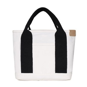 Detail of white canvas tote bag with black handles and a khaki leather side label