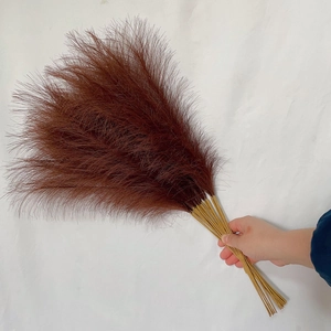Detail of hand holding fluffy 55cm dark brown artificial pampas grass in boho style