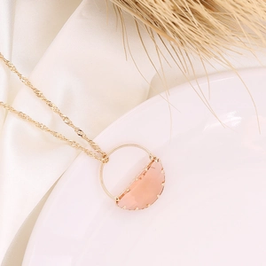 Elegant gold chain necklace with pink stone pendant on white silk and ceramic plate