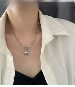 Close-up of a minimalist silver beaded necklace with a round polished pendant on a model