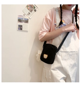 Detail of black corduroy mini crossbody bag with brown bear embroidery and plush charm